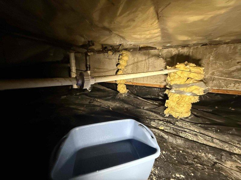Responded to callback for non-operational HVAC unit with water accumulation following recent water safety device installation. Upon inspection, identified active condensate leak causing water to collect in bucket. Accessed interior unit compartment and crawl space area to trace leak source along condensate drain line and PVC piping connections. Examined water safety device installation, drain pan, and associated plumbing components. Documented conditions with photos showing unit interior, drain components, and crawl space piping layout for diagnostic purposes and repair verification.