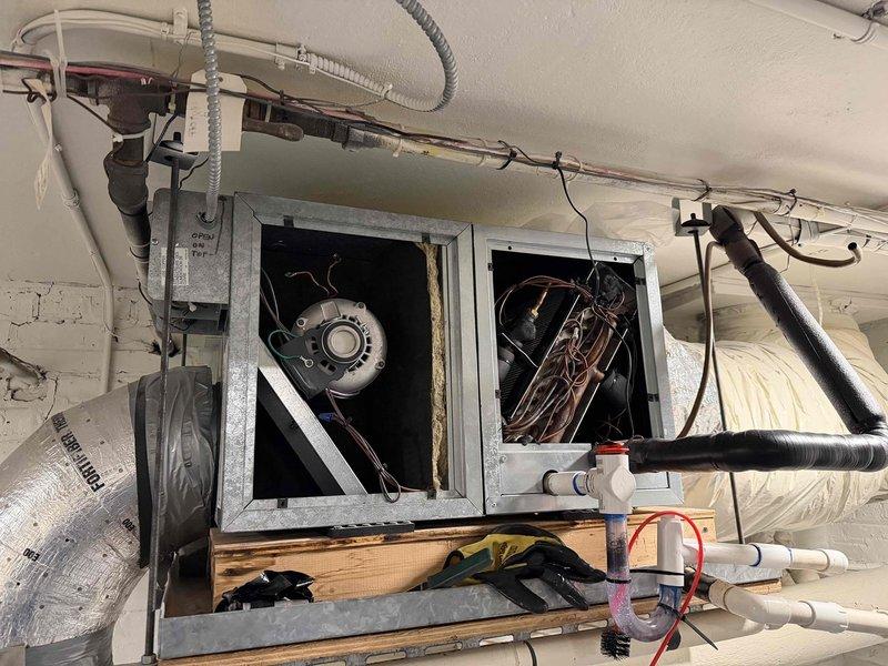Responded to no-cooling call with reported chemical odor emanating from Unico high-velocity air conditioning system in basement. Upon inspection, accessed blower compartment and air handler unit to investigate odor source and system malfunction. Performed visual inspection of blower motor assembly, electrical connections, and evaporator coil section. Identified potential refrigerant leak or electrical component failure as source of chemical smell. Documented system condition with interior compartment showing blower motor, wiring connections including ground wire routing, and control components. Inspected attic-mounted air handler with open access panels revealing blower assembly and copper refrigerant lines. Examined ductwork connections, insulated refrigerant piping, and shutoff valves for proper operation and leak indicators.