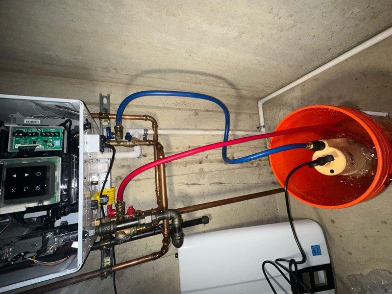 Performed maintenance on tankless water heater system including descaling flush procedure using circulation pump and cleaning solution as evidenced by bucket collection system with chemical hoses connected to service valves. Conducted diagnostic testing of unit operation and inspected electrical control board, display panel, and associated wiring connections for proper function. Recommended future flush service to maintain optimal performance and prevent mineral buildup in heat exchanger.