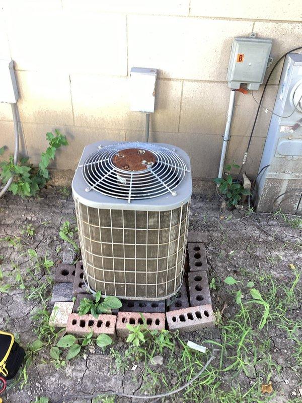 Completed comprehensive AC tune-up on 23-year-old outdoor condensing unit addressing high humidity concerns in apartment. Performed full system inspection, cleaned condenser coils, checked electrical connections and capacitor functionality, verified refrigerant levels, and tested system operation. Unit showed signs of age with visible corrosion on fan grille and accumulated debris, but all components were serviced and system restored to proper working condition.