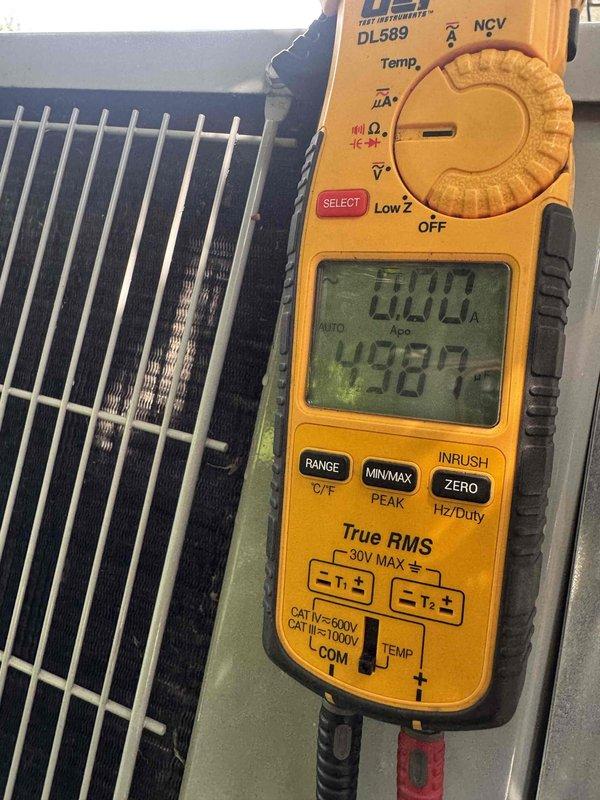 Performed comprehensive air conditioning maintenance and system diagnostics. Conducted electrical measurements at the outdoor condenser unit using a True RMS digital multimeter to verify proper voltage and amperage levels. Inspected condenser coil fins for debris accumulation and airflow restrictions, noting some discoloration between coil slats. Measured indoor air handler temperature readings, recording 50.3°F at the evaporator coil to confirm proper refrigerant charge and system performance. Documented all findings with photographic evidence for maintenance records.