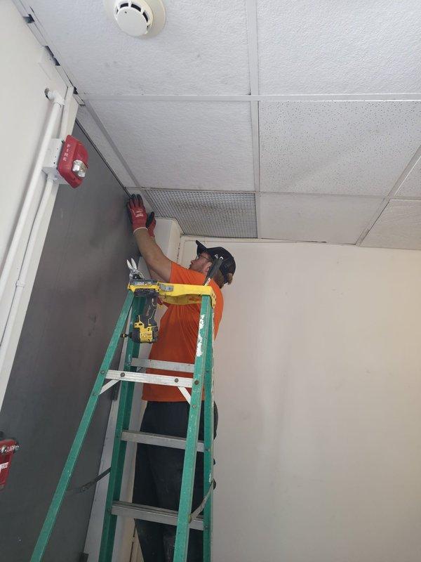 Responded to service call for ceiling tile repair in back office area near rear door. Upon arrival, accessed mechanical room to inspect HVAC system and verify proper operation of Carrier air handler unit. Confirmed clean air filter installation and proper equipment function. Proceeded to back office location where ceiling tile damage was reported. Set up ladder and safety equipment, then removed damaged acoustic ceiling tile from drop ceiling grid system near ventilation grille. Installed replacement ceiling tile, ensuring proper fit within existing grid framework and alignment with adjacent tiles and HVAC components. Verified smoke detector remained undisturbed and all ceiling penetrations were properly sealed. Documented conditions with photographs before completing work. Site left clean with all damaged materials removed and ceiling system restored to proper appearance and function.