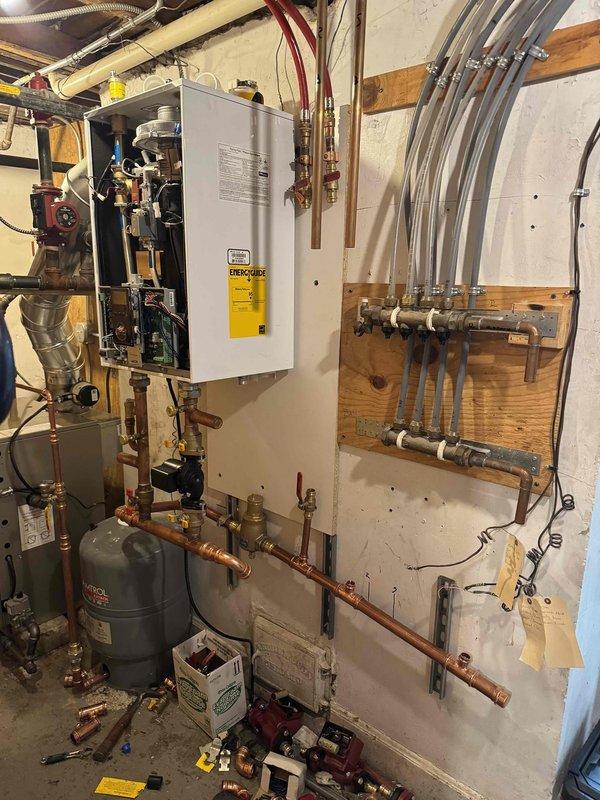 Completed full replacement of residential heating system including installation of new boiler and tankless water heater over a two-and-a-half-day period. Removed existing equipment and installed tan metal boiler unit with copper piping, red circulator pumps, pressure gauges, and proper black iron gas piping with brass valves and fittings. Mounted white wall-hung tankless unit with copper supply lines, installed gray expansion tank, and integrated PEX distribution manifold system for hydronic heating zones. All equipment secured to code with proper venting, verified system pressurization, tested all safety controls, and confirmed operational performance of both heating and domestic hot water systems.