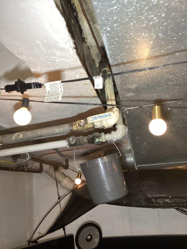 Responded to basement water leak inspection. Upon arrival, located active leak in main water line piping system in basement ceiling area. Leak identified at pipe fitting connection point, unrelated to HVAC system. Documented existing conditions with photographic evidence showing PVC piping configuration, electrical wiring proximity, and temporary collection bucket in place. Observed secondary damage to adjacent wall structure with exposed framing and drywall deterioration resulting from water intrusion. Provided assessment and recommendations for repair of compromised pipe connection and restoration of damaged wall surfaces.