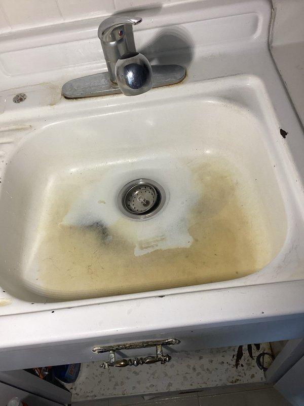 Responded to kitchen sink drainage issue with slow water flow. Accessed plumbing system through under-sink cabinet and inspected P-trap assembly, drain connections, and supply lines. Cleared obstruction from drain line, restoring proper water flow and drainage function. Verified all connections secure with no active leaks present. Documented existing sink staining and cabinet water marks from previous moisture exposure, though no current water damage observed. System tested and confirmed operational upon completion.