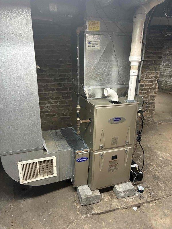 Completed furnace replacement in basement utility room, installing new Carrier brand unit with associated ductwork and plenum connections. Removed existing equipment and positioned new furnace on concrete block base, connecting white PVC condensate drainage and venting lines, electrical wiring to wall-mounted junction box, and integrating with existing silver metallic supply plenum and return air ductwork. Performed system pressure testing using digital manometer, verifying gas line connections at brass fittings and confirming proper operating pressures of 142/146 readings on dual port gauge, ensuring all electrical controls and safety switches functioning correctly before final commissioning of heating system.