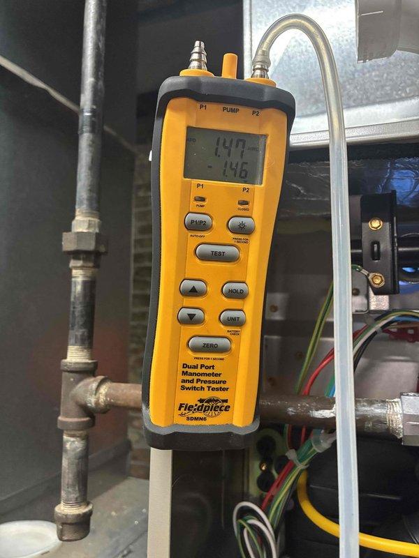 Completed furnace replacement in basement utility room, installing new Carrier brand unit with associated ductwork and plenum connections. Removed existing equipment and positioned new furnace on concrete block base, connecting white PVC condensate drainage and venting lines, electrical wiring to wall-mounted junction box, and integrating with existing silver metallic supply plenum and return air ductwork. Performed system pressure testing using digital manometer, verifying gas line connections at brass fittings and confirming proper operating pressures of 142/146 readings on dual port gauge, ensuring all electrical controls and safety switches functioning correctly before final commissioning of heating system.