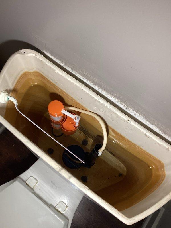 Completed comprehensive plumbing inspection with primary focus on toilet and bathroom faucet concerns. Upon inspection of the toilet tank, identified significant water discoloration with brownish rust-colored tinting throughout, indicating mineral deposits and potential aging pipe issues. Documented internal tank components including fill valve assembly with float mechanism and flush valve system, both showing signs of mineral buildup and staining on interior ceramic surfaces. The discolored water condition suggests possible corrosion in supply lines or water heater sediment transfer requiring further investigation and treatment.