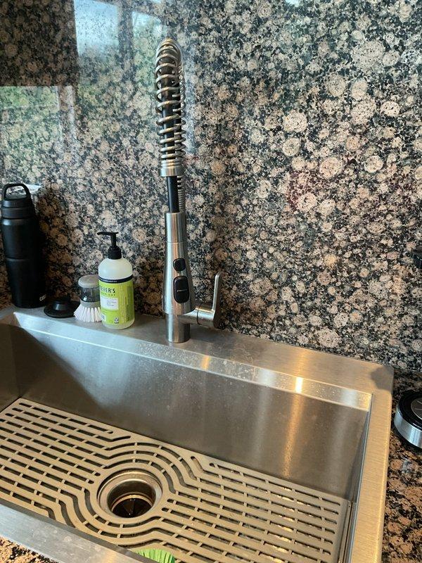 Completed plumbing inspection and diagnostic evaluation of kitchen sink system. Assessed all under-sink components including P-trap assembly, garbage disposal unit, supply lines, and drain connections. Documented existing installation featuring chrome P-trap with white threaded connectors, functional garbage disposal with discharge piping, and flexible water supply lines with proper fittings. Verified proper drainage function and photographed complete plumbing configuration for service records.