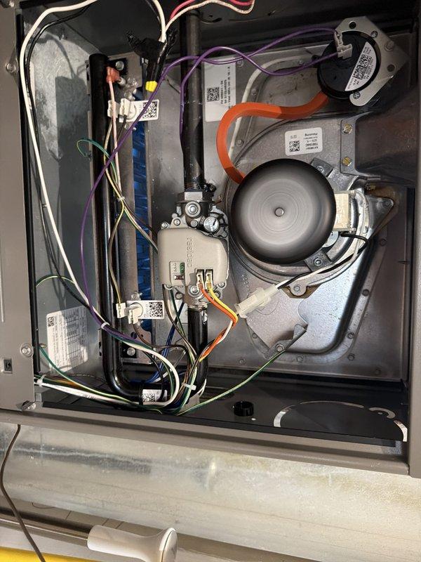 Completed tune-up on furnace and air conditioning system requiring telescopic ladder setup on back deck with second technician for safety support to access unit on pitched roof. Performed comprehensive inspection of furnace interior components including blower motor assembly, capacitor, gas valve, control board, and electrical connections. All wiring and connections found secure with proper routing throughout compartment. Measured supply air temperature at 73.3°F and discovered significant frost accumulation on evaporator coil and ductwork, indicating potential refrigerant charge issue or restricted airflow. Frost pattern showed irregular distribution with heavy crystalline buildup on metallic surfaces. Inspected all mechanical and electrical components within unit housing, verified proper labeling and manufacturer specifications visible on equipment. System components appeared clean and operational with no visible damage or deterioration noted during visual inspection.