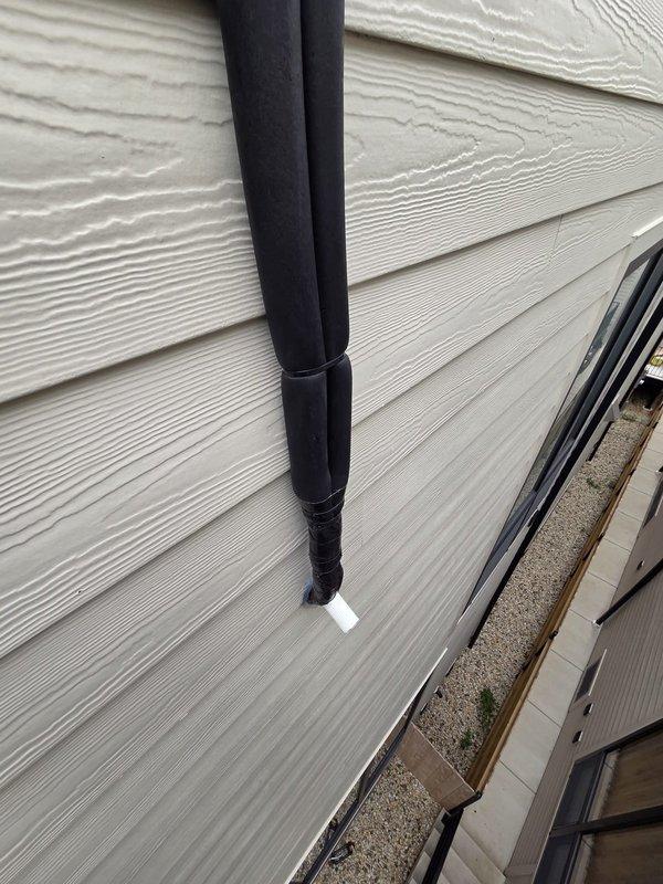 Completed site inspection and documented exterior drainage system condition. Observed black PVC condensate drain line with tape-wrapped sections running vertically along building exterior, terminating in white PVC elbow joint. Photographed drainage components and gutter system for service records.