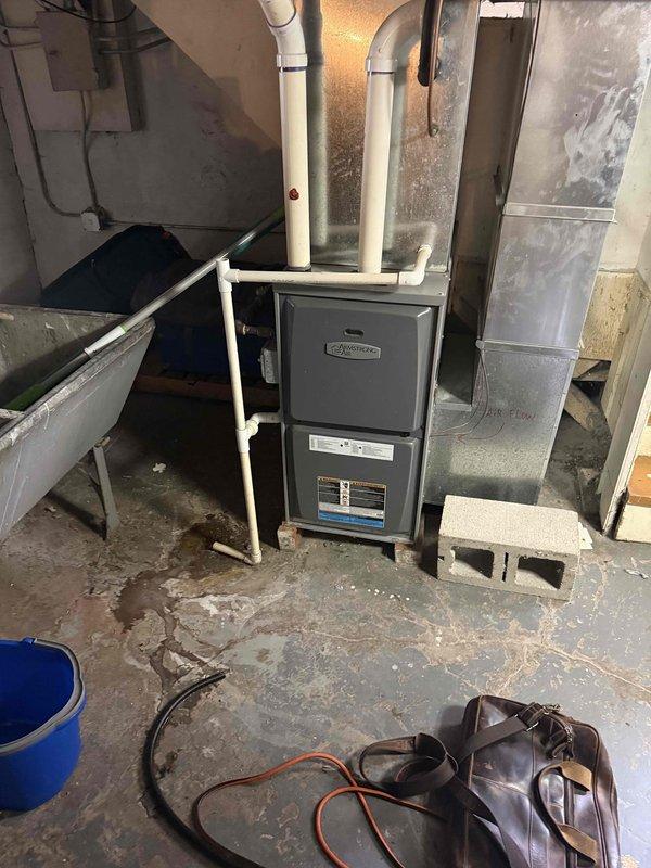 Conducted comprehensive assessment of 18+ year old furnace system experiencing inadequate cooling performance. Documented existing basement-installed HVAC unit with dark gray cabinet, PVC venting, and associated ductwork configuration. Performed detailed measurements of equipment dimensions and clearances using precision measuring tools. Evaluated complete system including furnace cabinet, supply and return ductwork, venting components, and installation environment. Photographed equipment nameplate data, unit positioning, ductwork connections, and mechanical room layout to develop accurate replacement specifications for full system estimate.