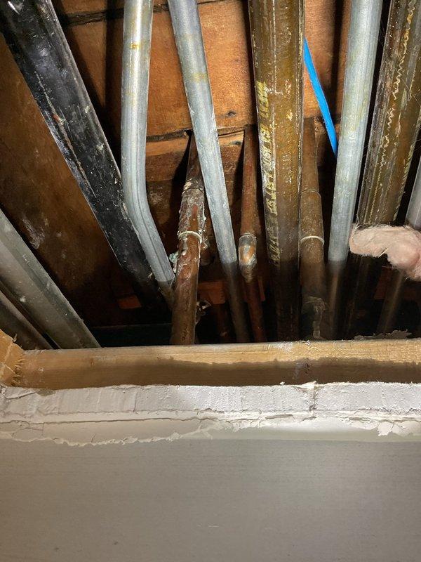 Responded to service call for corroded leaking shower pipe. Upon investigation, accessed plumbing lines through ceiling cavity and wall section to locate source of water intrusion. Identified deteriorated metal piping showing significant corrosion and active leak. Documented existing conditions including exposed conduit runs in ceiling space and plumbing configuration behind wall assembly adjacent to brick chimney structure. Provided assessment and photographic documentation of affected areas for repair recommendations.
