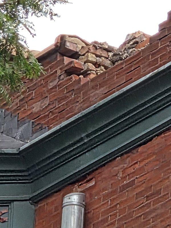 Conducted site inspection of exterior HVAC infrastructure and building structure. Documented significant chimney damage at roofline with collapsed masonry and displaced brickwork requiring immediate attention. Inspected and photographed vertical exhaust vent stack installation along brick exterior wall, confirming proper mounting bracket placement and structural integrity of the galvanized metal ductwork system.