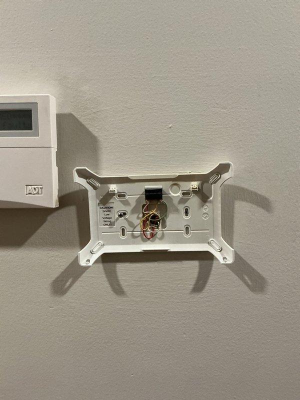 Completed return visit to replace thermostat. Removed existing thermostat from wall-mounted base plate and installed new unit, verifying proper wire connections at terminal screws including power, heating, cooling, and common wires. Tested system operation at air handler using diagnostic equipment to confirm proper communication between new thermostat and HVAC equipment, with temperature readings indicating normal system function at 129.9°F.