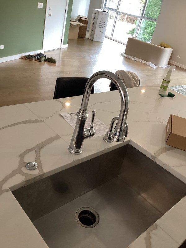 Replaced existing kitchen faucet with new timeless chrome fixture featuring high-arc spout and pull-down spray head. Installation completed on white marble-patterned countertop with undermount sink, including connection of water supply lines and verification of proper function for both main faucet and side spray attachment.