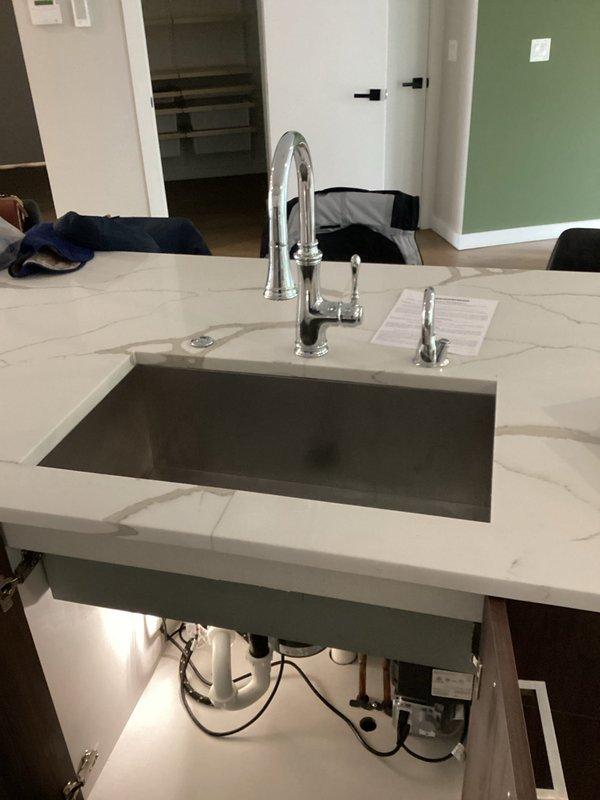 Replaced existing kitchen faucet with new timeless chrome fixture featuring high-arc spout and pull-down spray head. Installation completed on white marble-patterned countertop with undermount sink, including connection of water supply lines and verification of proper function for both main faucet and side spray attachment.