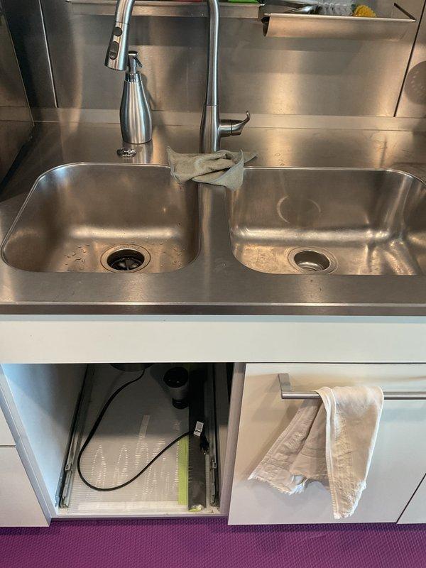 Responded to service call for kitchen sink drainage issue and secondary plumbing concern. Upon arrival, inspected commercial-style stainless steel double-basin sink installation with pull-down faucet. Accessed under-sink plumbing through cabinet doors to assess drainage system configuration. Observed P-trap assembly with chrome-plated drain pipes, garbage disposal unit on left basin, and water filtration system installed in cabinet space. Rodded out main drain line to clear obstruction causing slow drainage. Verified proper flow through both basins and confirmed P-trap connections were secure with no active leaks. Inspected secondary plumbing components including filtration cartridge and disposal unit connections. All drainage systems tested and functioning properly upon completion.