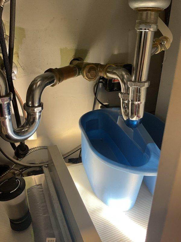Responded to service call for kitchen sink drainage issue and secondary plumbing concern. Upon arrival, inspected commercial-style stainless steel double-basin sink installation with pull-down faucet. Accessed under-sink plumbing through cabinet doors to assess drainage system configuration. Observed P-trap assembly with chrome-plated drain pipes, garbage disposal unit on left basin, and water filtration system installed in cabinet space. Rodded out main drain line to clear obstruction causing slow drainage. Verified proper flow through both basins and confirmed P-trap connections were secure with no active leaks. Inspected secondary plumbing components including filtration cartridge and disposal unit connections. All drainage systems tested and functioning properly upon completion.