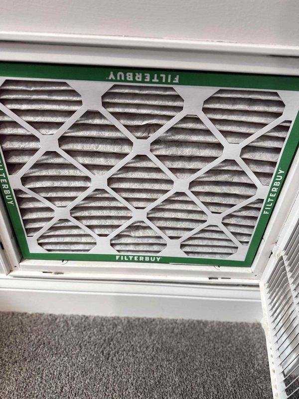 Responded to service call for air conditioning unit making unusual noise. Used telescopic extension ladder to access exterior-mounted window AC unit on second floor of residence. Upon inspection, identified source of operational sound concern. Documented condition of unit with photos and inspected return air filter, which showed moderate dust accumulation on pleated media but maintained structural integrity with proper seating in housing. Filter brand documented as Filterbuy with characteristic green border framing.