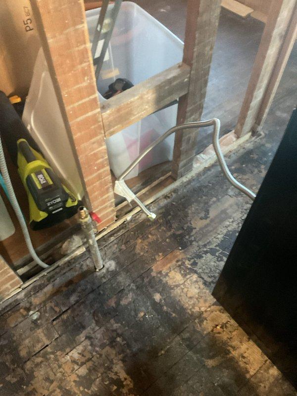 Completed gas range hookup and installation in residential property undergoing renovation with extensive fire or water damage to subfloor. Connected gas line to freestanding four-burner range with stainless steel controls in unfinished space with exposed framing, ensuring proper ventilation and code-compliant installation despite challenging site conditions.