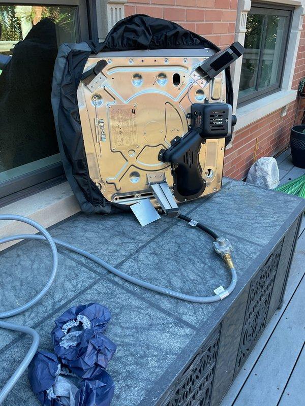 Conducted on-site evaluation for natural gas line modification to accommodate new pizza oven installation on outdoor patio area. Assessed existing gas hookup currently serving grill to determine feasibility of adding T-connector for dual appliance configuration. Documented copper gas line penetrations through brick wall, existing plumbing connections, and available workspace on composite deck surface for proposed installation work.