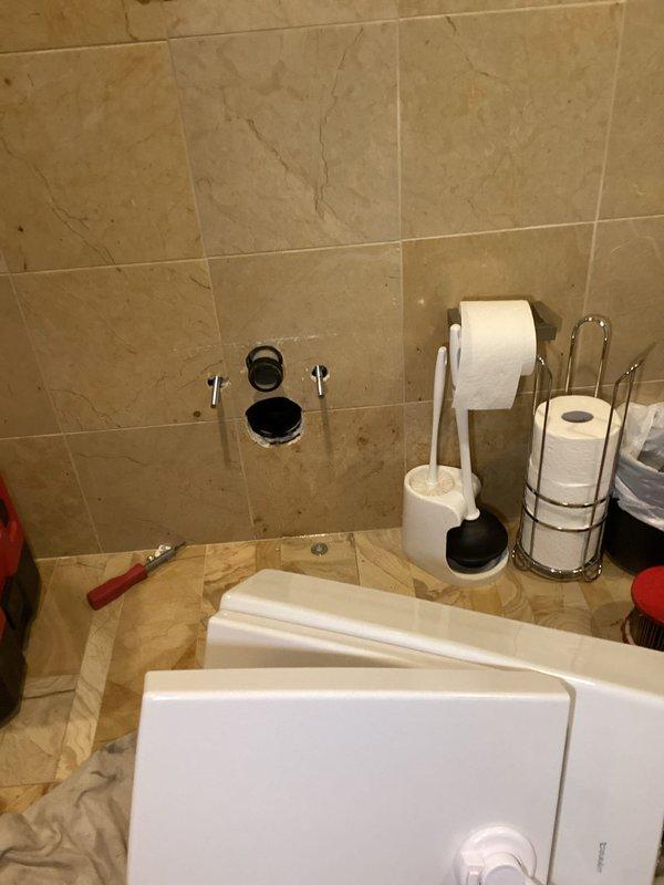 Returned for callback on previously serviced slow-draining toilet where issue has recurred. Inspected wall-mounted flush mechanism, rimless bowl toilet, and drainage system; documented conditions with photos showing modern bathroom installation with marble tile finishes. Assessed flush valve operation, water flow patterns, and potential blockage points to determine root cause of persistent slow drainage problem.