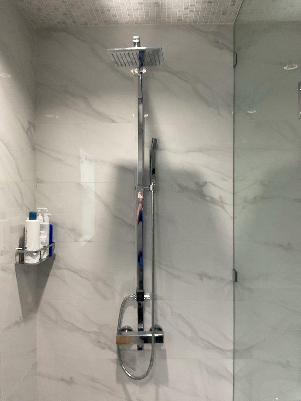 Completed shower cartridge replacement on chrome thermostatic mixing valve in modern tiled shower enclosure. Removed existing cartridge from wall-mounted control valve, installed new replacement cartridge, tested water temperature control and flow distribution between rain head and handheld shower attachment to verify proper operation of diverter system.