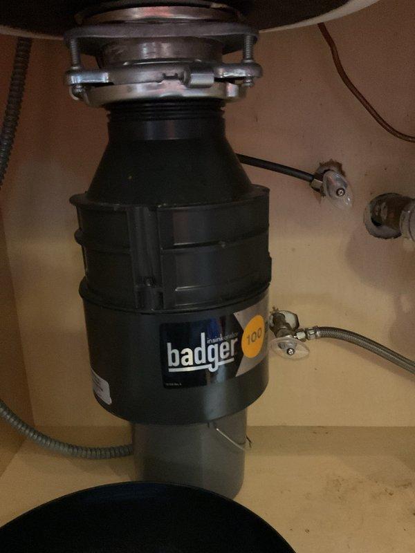 Responded to service call for leaking garbage disposal unit. Upon inspection, identified active water leak from Badger 100 model disposal that had previously experienced jamming issues. Assessed mounting assembly, drain connections, and discharge plumbing for source of leak. Found compromised seal at sink flange connection point. Evaluated overall condition of disposal unit and determined extent of water damage to surrounding cabinet area. Documented existing installation configuration including PVC drain lines, dishwasher discharge connection, and electrical connections. Provided assessment of disposal condition and recommended repair options to address the ongoing leak issue that had been present for multiple days.