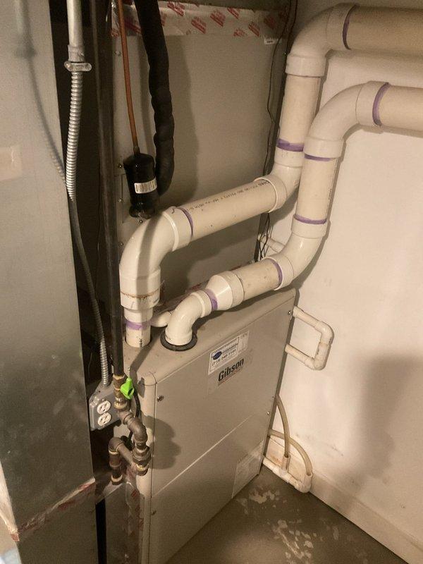 # HVAC Cooling System Repair - Condensate Drainage Issue

Responded to service call for water accumulation in basement during air conditioning operation. Upon arrival, inspected Gibson air handler unit and associated condensate drainage system. 

Identified improper drainage configuration in PVC condensate line assembly causing water backup. The existing piping network above the unit showed multiple connection points with potential for improper pitch or blockage. Assessed all elbows, joints, and horizontal runs for proper slope and drainage flow.

Cleared condensate line blockage and verified proper drainage function. Tested system operation by running cooling cycle and monitoring condensate flow through drain lines. Confirmed water was evacuating properly through drainage system without backup or overflow into basement area.

Verified thermostat operation showing system in off mode with indoor temperature reading 69°F. Checked electrical connections, including grounding and power supp