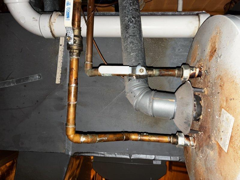 Conducted comprehensive site evaluation for tankless water heater conversion at residential property. Assessed existing tank-style water heater installation showing significant age-related deterioration with visible rust staining on exterior surface. Documented current plumbing configuration including copper supply lines, brass shutoff valves, white PVC discharge piping, and expansion tank. Evaluated utility room infrastructure including concrete block walls, available clearances, existing electrical service, gas connections, and ventilation requirements. Provided detailed estimate for complete removal of conventional storage tank unit and installation of new tankless water heating system with necessary upgrades to meet current code requirements.