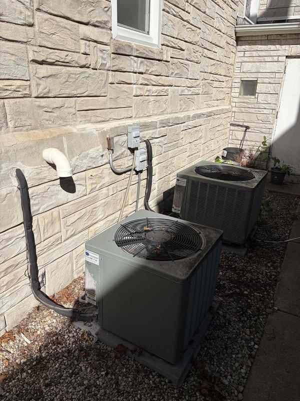 Completed furnace replacement for 16-year-old unit that was shut down and no longer operational. The existing furnace had easy access for removal and installation. Documented existing ductwork measurements showing 13-inch diameter supply plenum, and photographed exterior HVAC equipment including dual air conditioning condensers positioned on gravel pad with proper refrigerant line sets and drainage components connected to the building exterior.