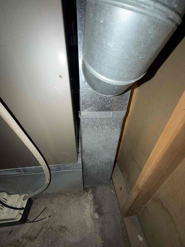 Conducted comprehensive assessment of existing HVAC system in basement utility area for full system replacement estimate. Customer expressed interest in upgrading to Carrier Performance series equipment for both heating and cooling components. Evaluated current furnace installation, ductwork configuration, and air conditioning requirements. Documented existing galvanized metal duct system with vertical runs and rectangular transitions, noting dust accumulation on surfaces. Assessed basement mechanical room layout including concrete floor conditions, exposed framing, and existing utility connections. Photographed current furnace unit with front grille panel, supply ductwork extending from unit top, and ceiling-mounted distribution system secured with metal straps. Reviewed electrical wiring paths, structural clearances, and access points for equipment replacement. Prepared specifications for Carrier Performance system installation including furnace and air conditioning components matche