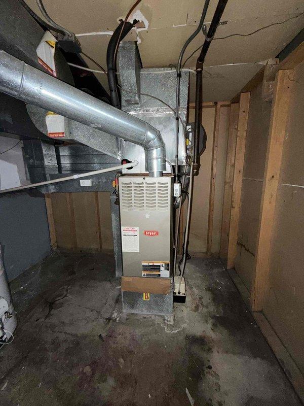 Conducted comprehensive assessment of existing HVAC system in basement utility area for full system replacement estimate. Customer expressed interest in upgrading to Carrier Performance series equipment for both heating and cooling components. Evaluated current furnace installation, ductwork configuration, and air conditioning requirements. Documented existing galvanized metal duct system with vertical runs and rectangular transitions, noting dust accumulation on surfaces. Assessed basement mechanical room layout including concrete floor conditions, exposed framing, and existing utility connections. Photographed current furnace unit with front grille panel, supply ductwork extending from unit top, and ceiling-mounted distribution system secured with metal straps. Reviewed electrical wiring paths, structural clearances, and access points for equipment replacement. Prepared specifications for Carrier Performance system installation including furnace and air conditioning components matche
