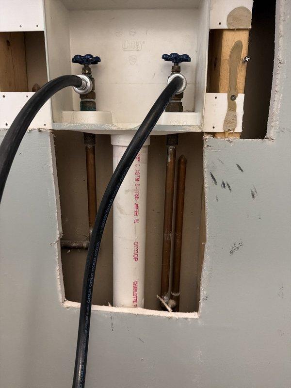 Replaced existing grey laundry box with new white Oatey outlet box assembly, installing two shut-off valves with quarter-turn handles (red and blue) connected to existing copper supply lines and PEX tubing. Installation completed with black flexible supply lines extending from mounted valves, providing proper water supply connections for washing machine hookup.