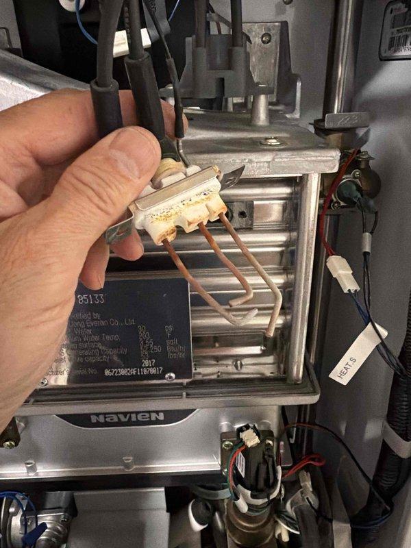 Responded to service call for 8-year-old Navien radiant floor heating system in lower level experiencing operational issues. Upon inspection, identified failed thermal fuse component showing visible discoloration and burn marks indicating electrical failure. Removed defective ceramic thermal fuse from unit and replaced with OEM component to restore proper system operation. Verified all electrical connections secure and tested unit functionality. System now operating within normal parameters and providing heat to radiant floor zones as designed.
