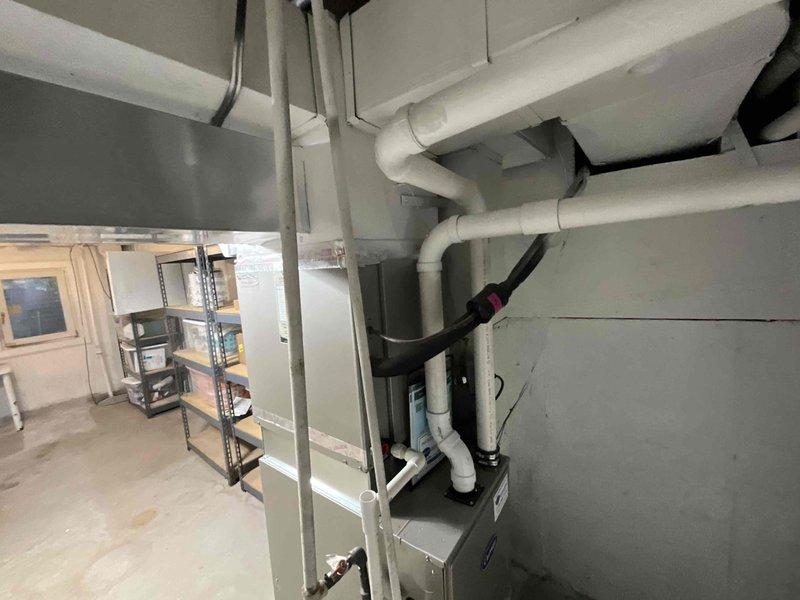 Conducted on-site evaluation of existing 15-year-old air conditioning system for replacement estimate. Inspected outdoor condenser unit positioned on concrete pad against exterior brick wall, noting weathered equipment and overgrown vegetation requiring clearance. Assessed indoor HVAC components in mechanical room, including furnace unit and existing ductwork configuration with PVC piping system. Documented current system specifications and spatial requirements, photographed equipment and installation areas, and provided comprehensive replacement options for new cooling system to meet anticipated 2026 replacement timeline.