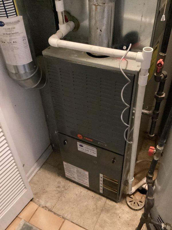 Responded to a no-cool complaint on a Trane gas furnace/air handler installation. Inspected the equipment with the front panel removed and evaluated the gas valve, burner assembly, control wiring, and condensate drain piping to diagnose the cause of the unit not energizing. Noted rust streaking on the galvanized flue pipe near the cabinet connection, which should be monitored for possible moisture or condensation issues.