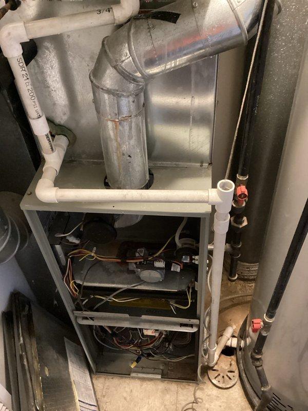 Responded to a no-cool complaint on a Trane gas furnace/air handler installation. Inspected the equipment with the front panel removed and evaluated the gas valve, burner assembly, control wiring, and condensate drain piping to diagnose the cause of the unit not energizing. Noted rust streaking on the galvanized flue pipe near the cabinet connection, which should be monitored for possible moisture or condensation issues.