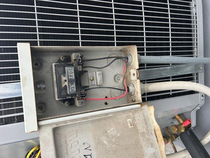 Responded to a warranty call for an intermittent no-cooling condition on a recently replaced AC system. Inspected the outdoor condensing unit's electrical disconnect and control section, finding dust accumulation and corrosion on the disconnect enclosure and conduit entries, with the contactor, run capacitor, and wiring harness showing no visible damage or failure. The system was operating normally following a customer breaker reset, and the electrical connections should be monitored for recurrence of a tripped breaker.