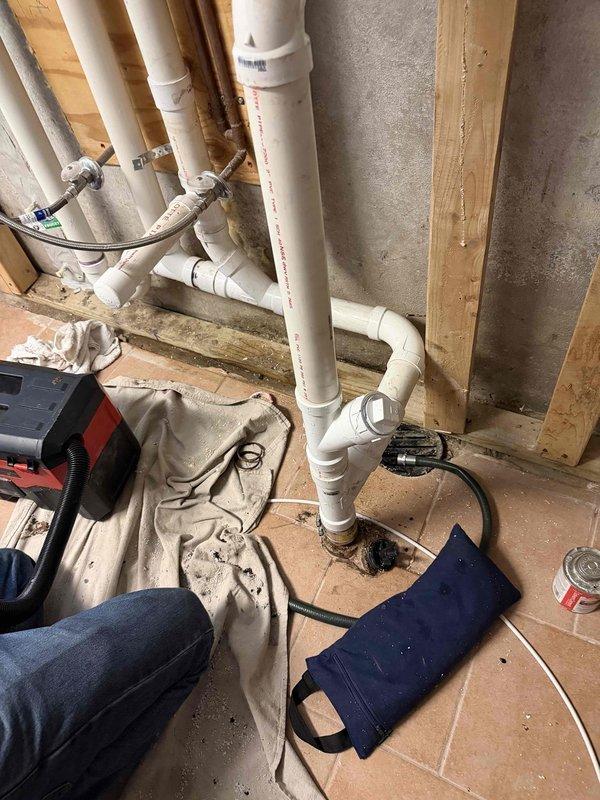 Re-piped the laundry sink drain using new PVC drain piping with a wye fitting and cleanout, tied into the existing floor drain and secured along the framed wall. Replaced the laundry supply valves and angle stops with new fittings, reconnected the flexible supply lines, and protected the work area with drop cloths throughout the repair.
