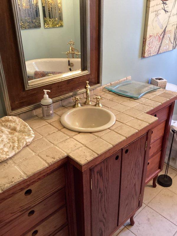 Inspected two bathrooms to assess scope for replacing both lavatory sink drain assemblies, replacing the existing one-piece toilet, and repairing a persistent drip at the vanity faucet. Evaluated the brass two-handle faucet and drop-in sink for worn cartridges or washers and drain stopper condition, and checked the toilet's floor seal and supply connections for caulk discoloration or leakage. Documented fixtures and existing conditions with photos to prepare an accurate quote for the repairs and replacements.