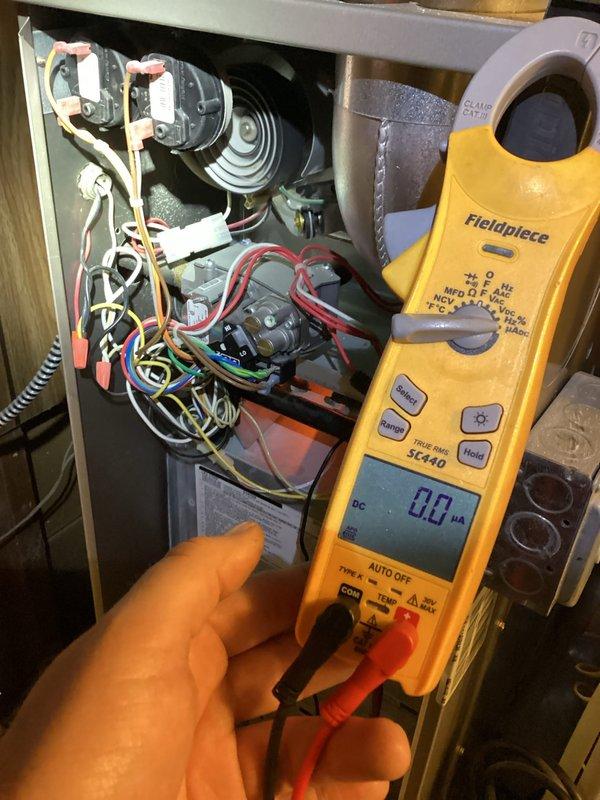 Responded to a no-heat call on a 7-year-old gas furnace and opened the cabinet to inspect the gas valve, pressure switches, inducer assembly, and control wiring. Used a clamp meter in µA/DC mode to test flame sensor circuit current (reading 0.0 µA, indicating no flame signal), and inspected the wiring harness and panel/junction box area for faults, with no visible damage, corrosion, or loose connections observed. Heating system was diagnosed for flame sensing and ignition sequence issues.