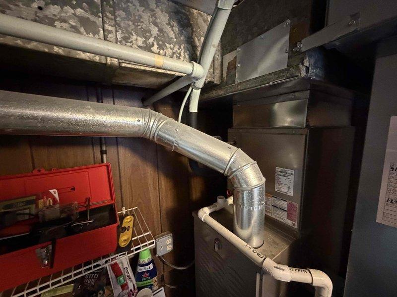 Evaluated a 9-year-old gas furnace in a utility closet for replacement, inspecting the flue venting, plenum and ductwork, condensate drain line, and electrical connections, with no significant rust, frost, or damage observed. Assessed the existing installation and access routes, including the staircase leading to the equipment space, to prepare a replacement quote.