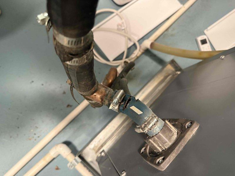 Performed an on-site evaluation and prepared a replacement quote for a Triangle Tube boiler. Inspection revealed a cracked blue rubber hose connection with a corroded copper fitting, mineral buildup, and rust staining at the boiler's flanged fitting, and clearance measurements were taken at the existing unit location to confirm sizing and installation requirements for the new boiler.