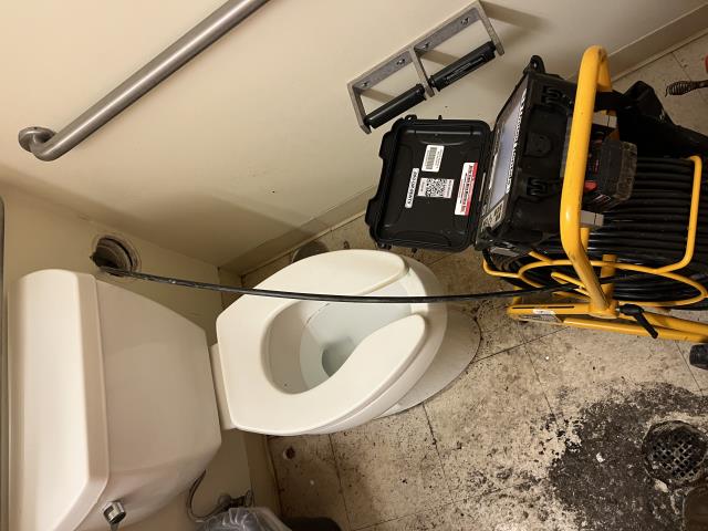 Upon arrival, our technician was greeted by the store manager, who led us to the restrooms experiencing issues. Upon entering the men’s bathroom, our technician immediately noted dried sewage on the floor and a strong septic odor.
Further investigation led to the clean-out located behind the toilet, which was accessed by removing the wall cover and clean-out cap. The technician then ran the inspection camera, which became fully submerged in standing water within 8 feet. Continuing the inspection, an obstruction was encountered approximately 25 feet downstream.
The camera was removed, and our technician proceeded to snake the drain line. Snaking the line revealed a blockage caused by feminine hygiene products. Once cleared, both toilets were tested and confirmed to be flushing and functioning at 100%.
A follow-up camera inspection confirmed that, while both fixtures were operating properly, standing water remained in the line. The camera again became fully submerged with limited visi