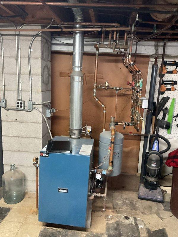 Evaluated basement heating system for relocation of two boiler registers. Inspected existing copper piping, flexible metal ducting, and connections to blue boiler unit with attached expansion tanks. Provided quote for register relocation work, including necessary modifications to existing ductwork.
