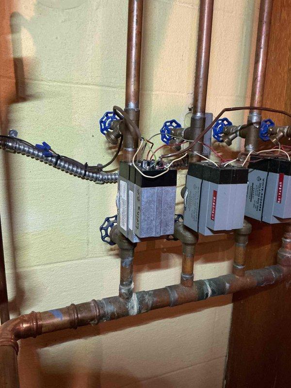 Performed diagnostic inspection on recently installed boiler system to address customer concern about a leaking valve. Identified issue with one of the zone valve assemblies in the hydronic heating system. Photos documented the multiple zone control setup with copper supply/return lines and electronic control boxes for the various heating zones.