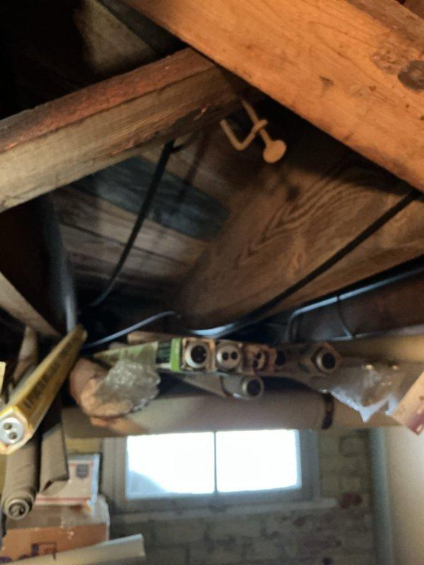 Performed inspection of hot water tank and identified severely corroded exhaust vent. Documented condition with photos showing the deteriorated ventilation system in relation to surrounding structural elements and plumbing infrastructure. Recommended replacement of rotted exhaust components to prevent potential carbon monoxide hazards.
