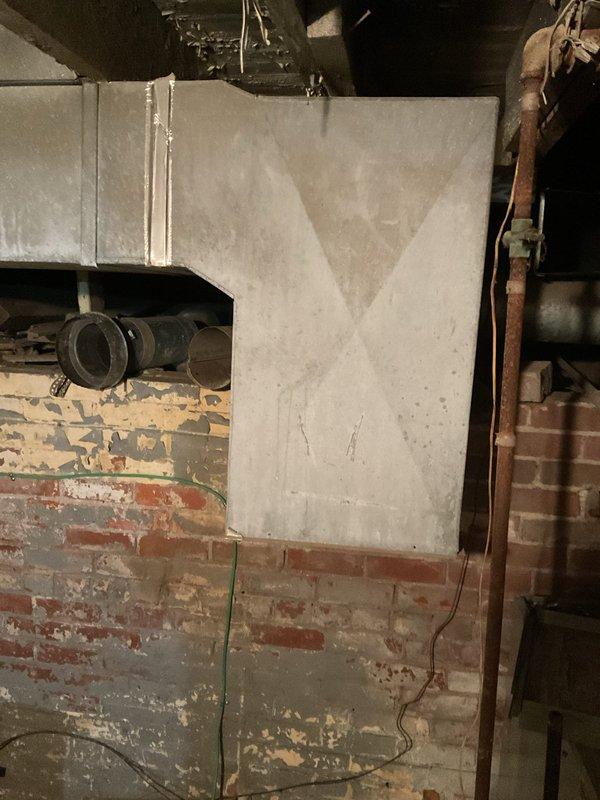 Performed comprehensive assessment of two aging furnaces located in basement utility area with exposed brick walls and deteriorating infrastructure. Evaluation revealed outdated units with accessible internal components requiring complete replacement. Documented existing ductwork configuration, including rectangular sheet metal junction and connecting pipes, to ensure proper sizing and compatibility with replacement systems.